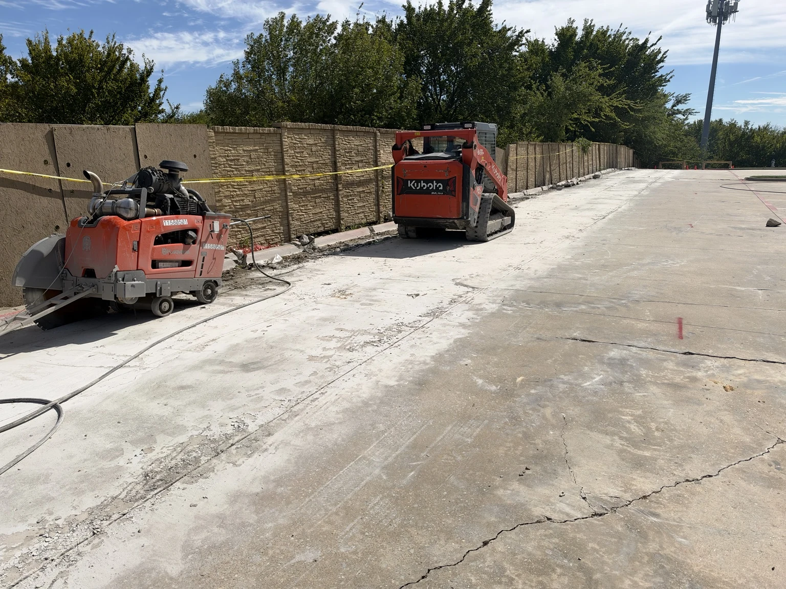 Concrete saw and compact track loader staged on existing commercial pavement